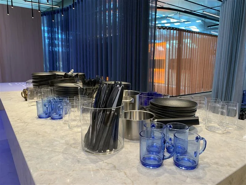Theke in Marmoroptik in einer BORA-Ausstellung mit Tellerstapeln, Gläsern, blauen Glastassen, Besteck und Töpfen