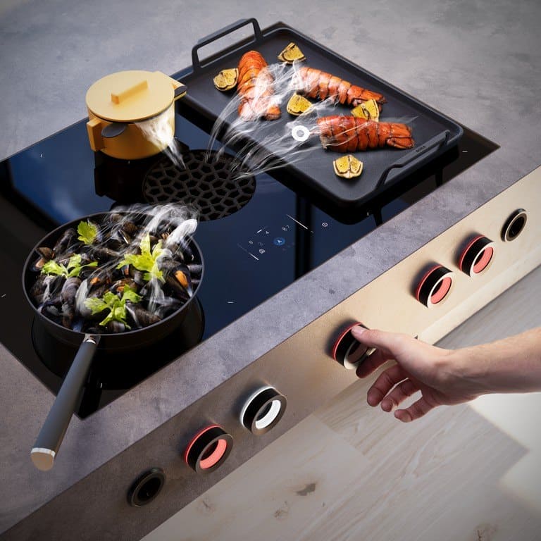 Hand dreht einen rot leuchtenden Knebel unter einem BORA X Pure Max, auf dem Kochfeld Grillpfanne und Topf
